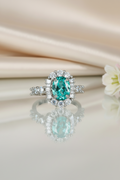 Ring with a green gemstone on a reflective surface with flowers in the background
