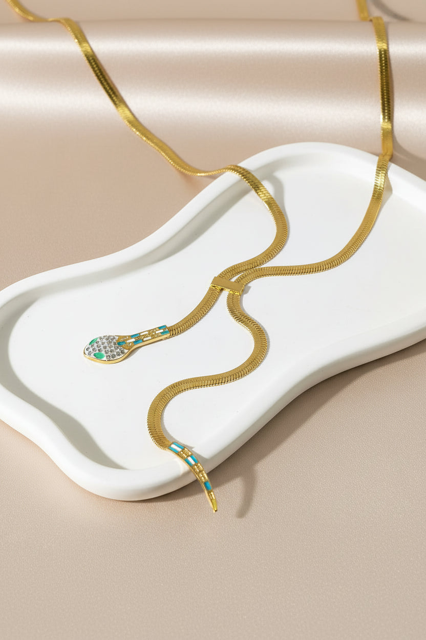 Gold snake-shaped necklace with gemstones on a marble surface