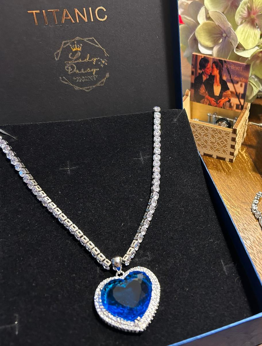 Titanic-themed necklace with blue heart pendant on a black box and blue Titanic pouch.