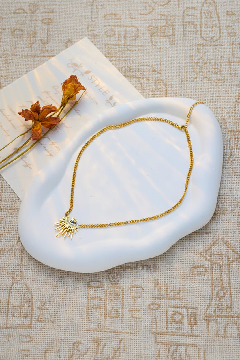Gold necklace with a sun design on a white stone surface with dried flowers.